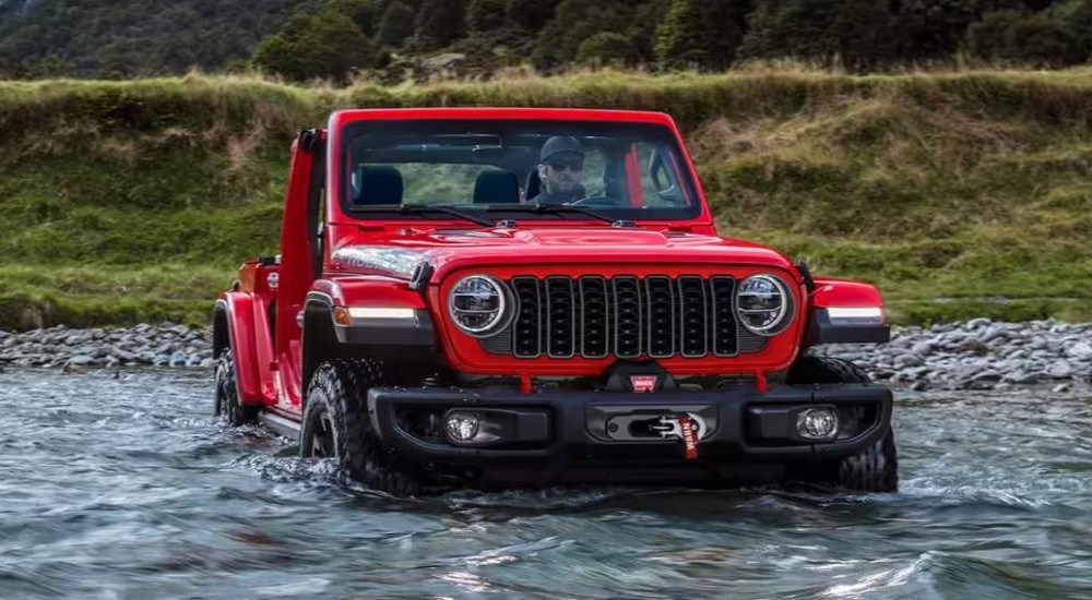 Red 2026 Jeep Wrangler Rubicon driving through a shallow river.