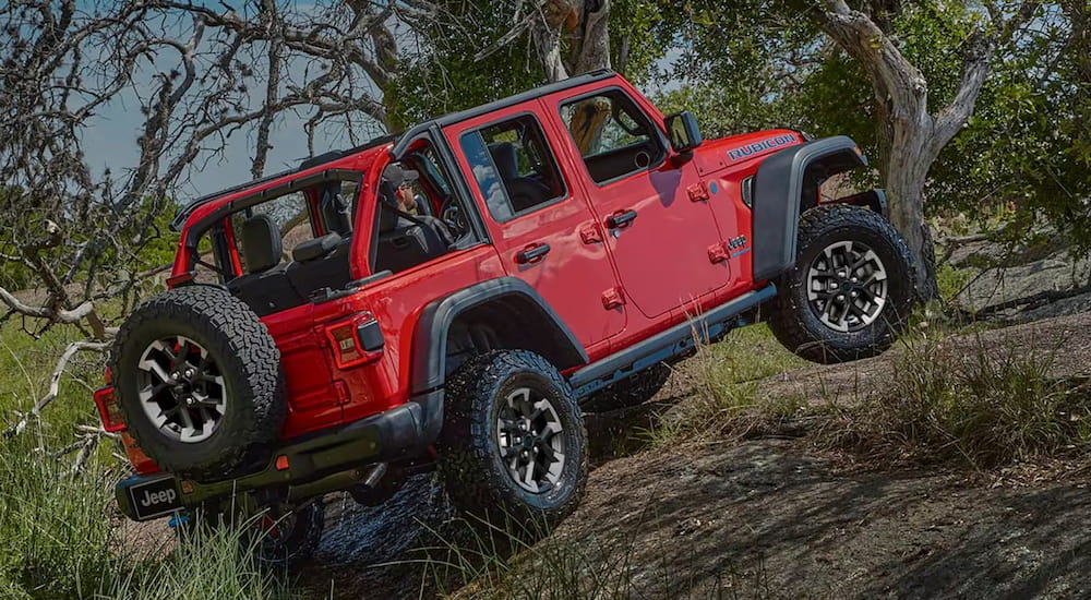 Rear of a red 2026 Jeep Wrangler driving off-road up a hill.
