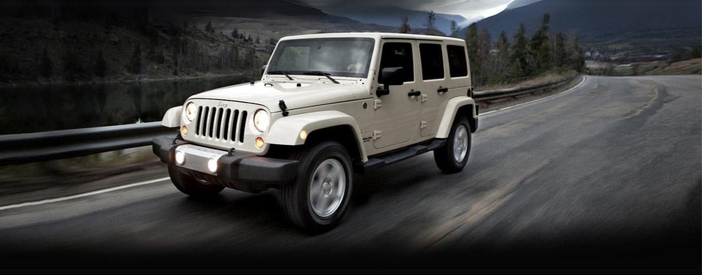 White 2011Jeep Wrangler Unlimited driving to see a used Jeep for sale near Brighton