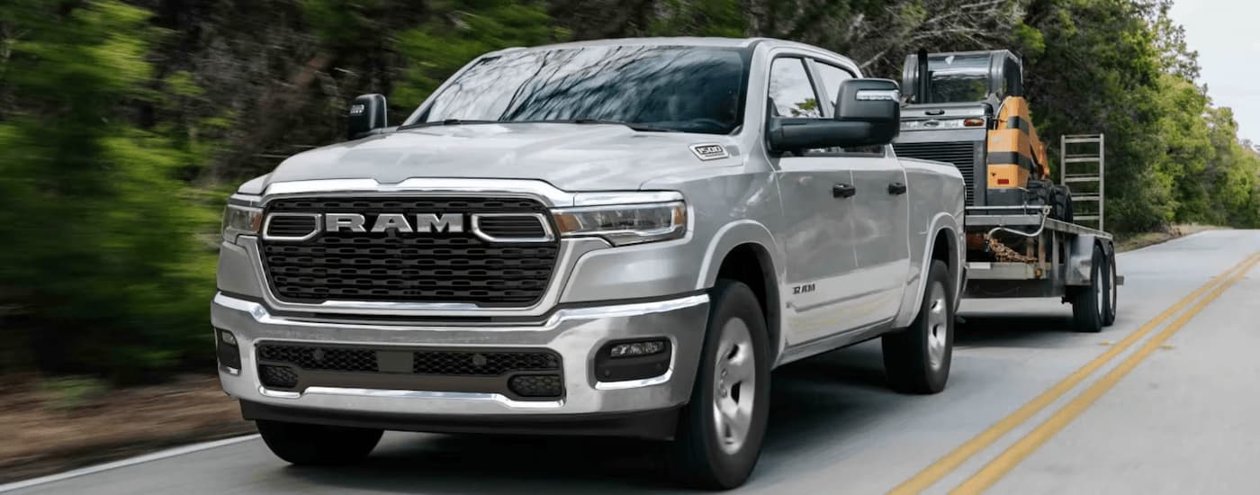 Silver 2025 Ram 1500 Big Horn towing heavy machinery on a trailer