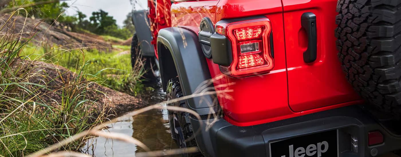 Rear view of a red 2026 Jeep Wrangler driving through a river