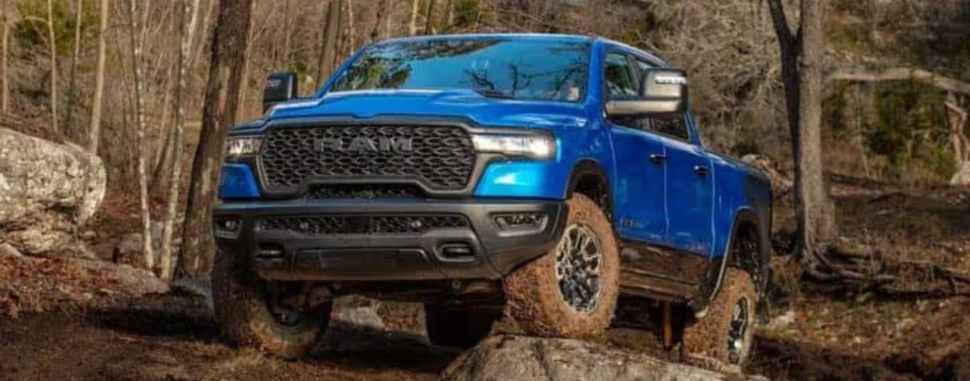 A blue 2025 Ram 1500 Rebel is off-roading on muddy trail.