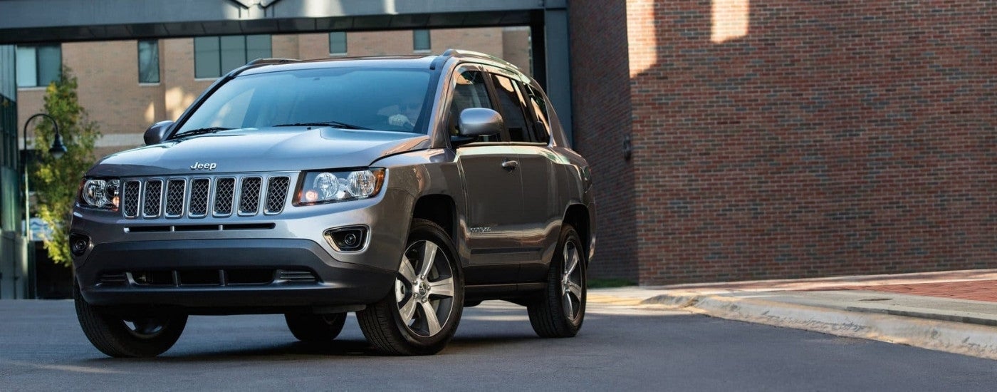 A silver 2017 Jeep Compass High Altitude parked in front of a brick building.