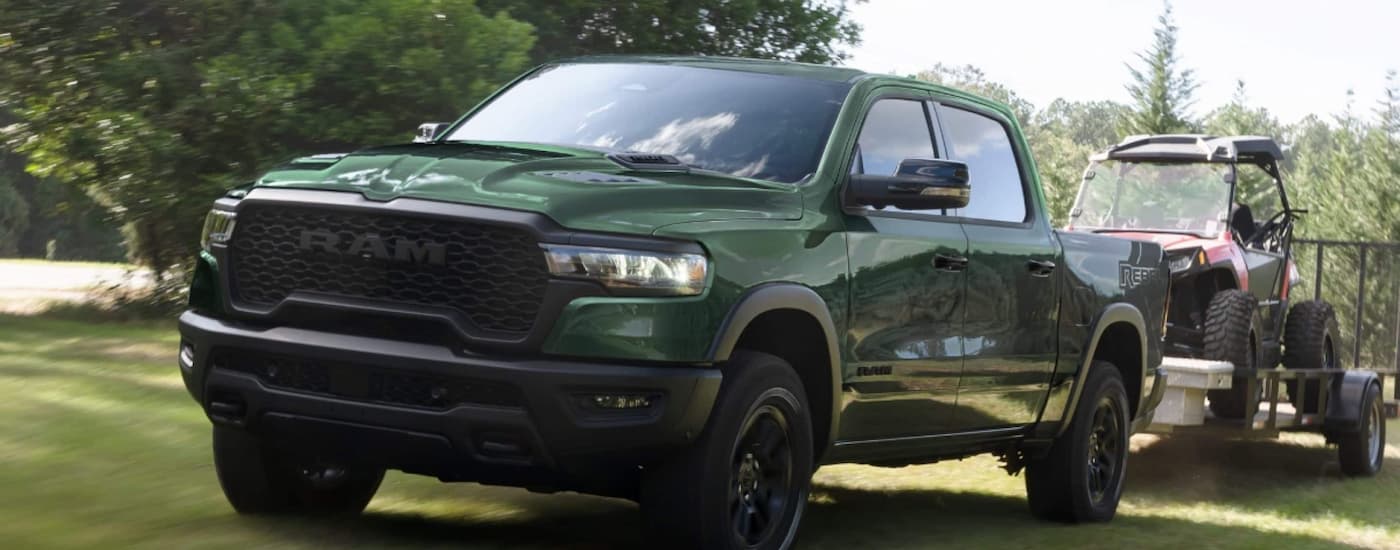 Green 2025 Ram 1500 towing an ATV off-road.